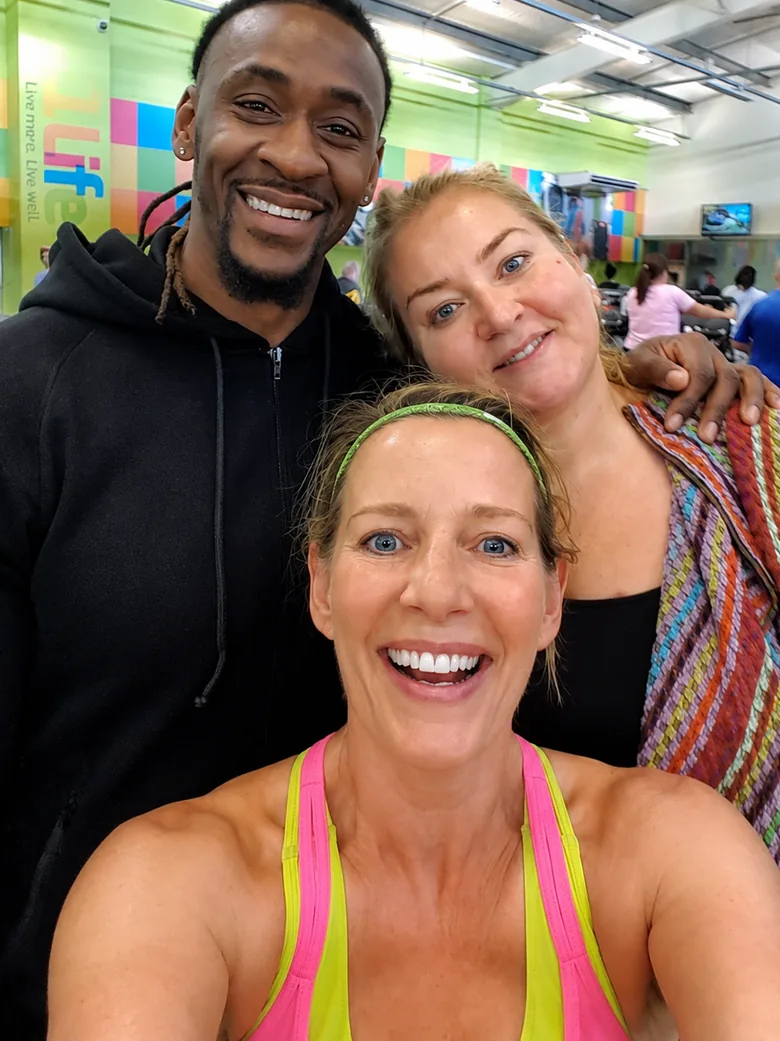 Three people smiling to camera together in a gym.